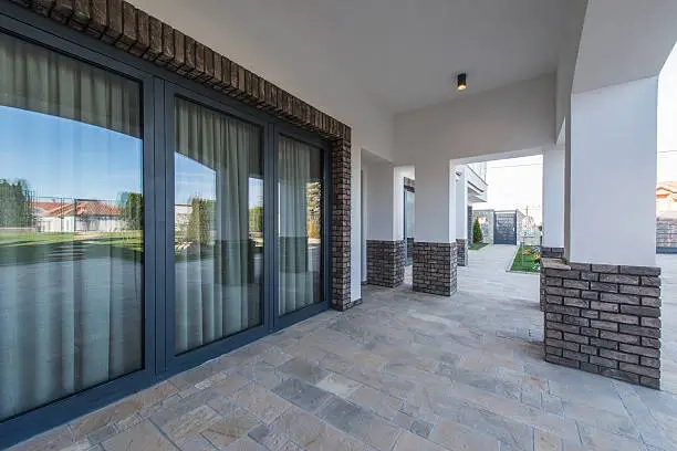 Spacious tiled patio with brick and white pillars.