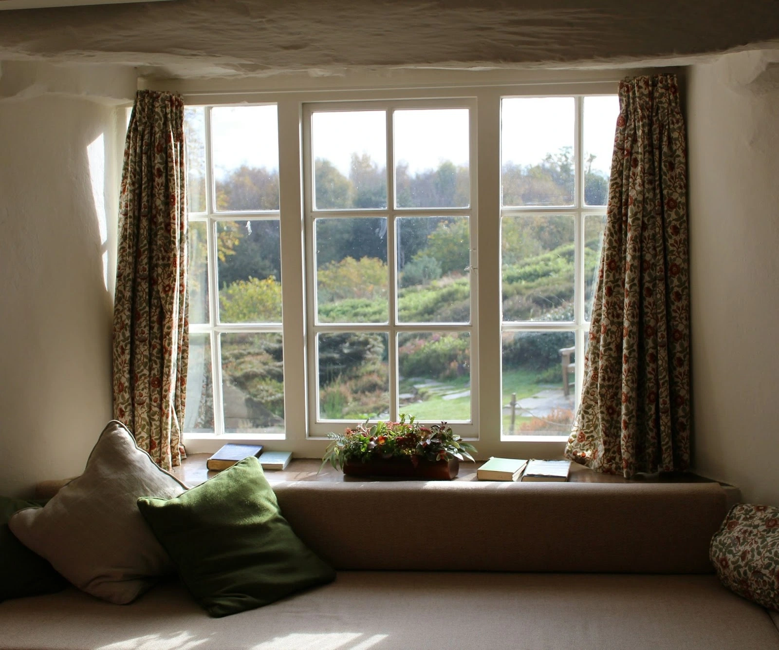 Cozy window seat with pillows, books, and a garden view.